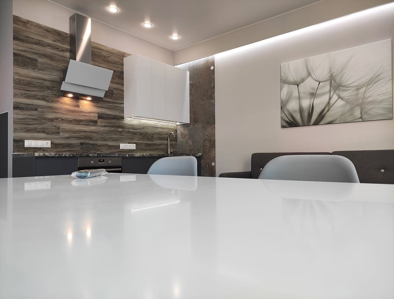 Столовая зона с белой столешницей и видом на кухню с подсветкой и вытяжкой