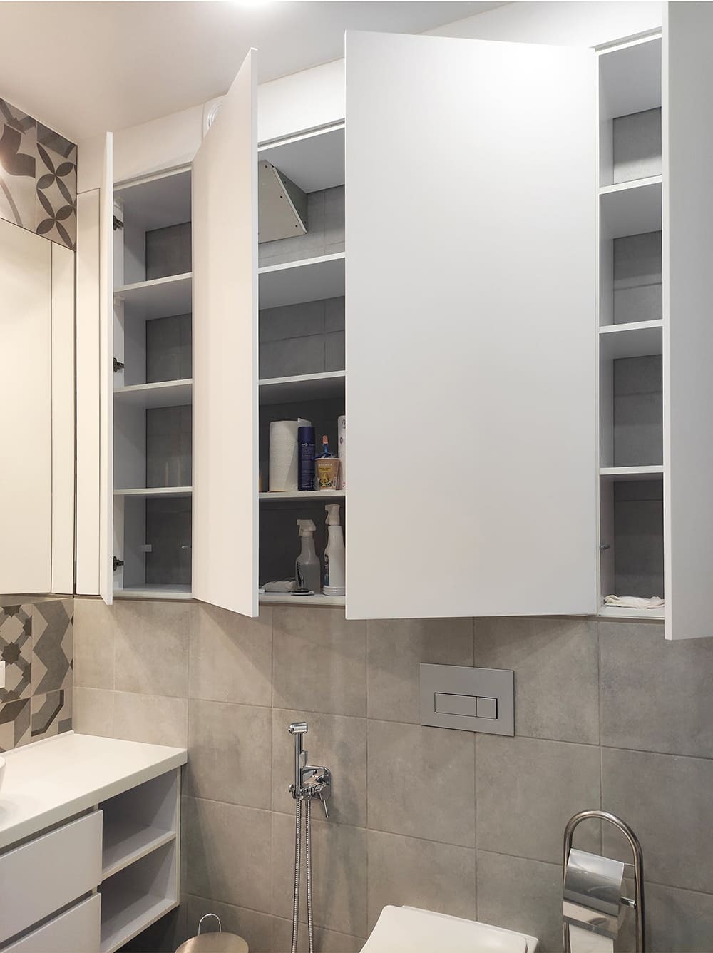 Открытые шкафы в санузле с полками для бытовой химии и серой плиточной отделкой