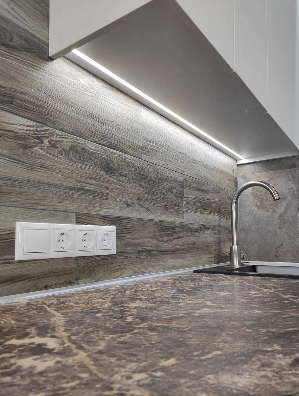 Крупный план дизайн-проекта кухни с белыми верхними шкафами, светодиодной подсветкой и древесным фартуком