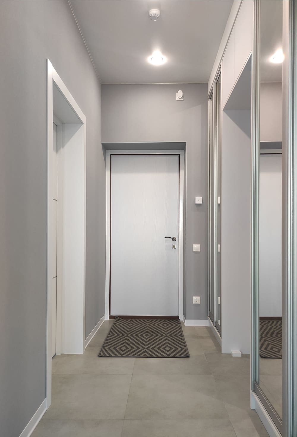 Входная зона квартиры с зеркальными фасадами шкафов, серыми стенами и ровным потолочным светом