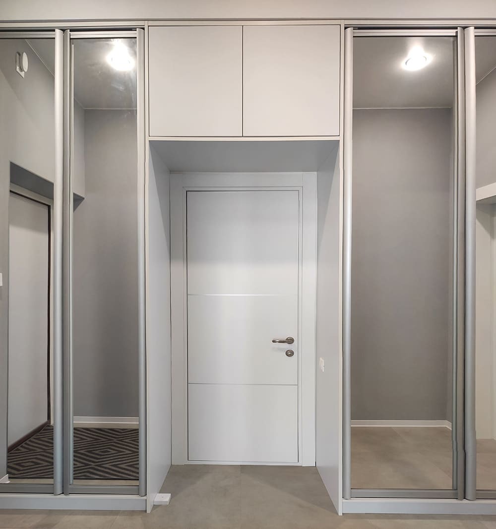 Зеркальный шкаф-купе в прихожей с белой дверью и современной отделкой стен