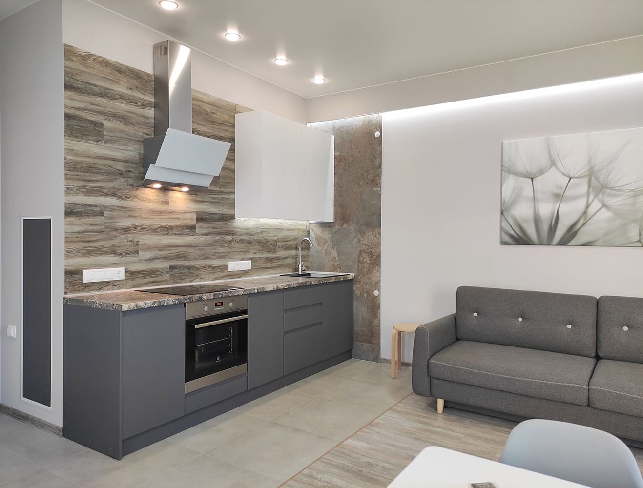 Интерьер современной кухни-гостиной с серыми нижними шкафами, белыми верхними модулями и древесным фартуком