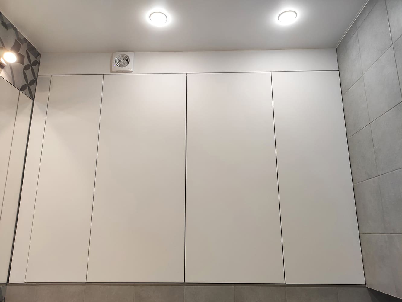 Интерьер ванной с высокими белыми фасадами и серой плиткой