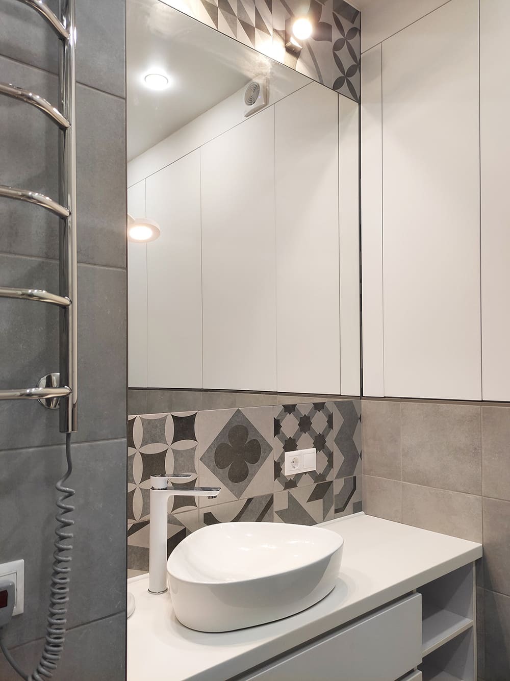 Санузел с зеркальными шкафами и декоративной геометрической плиткой под раковиной