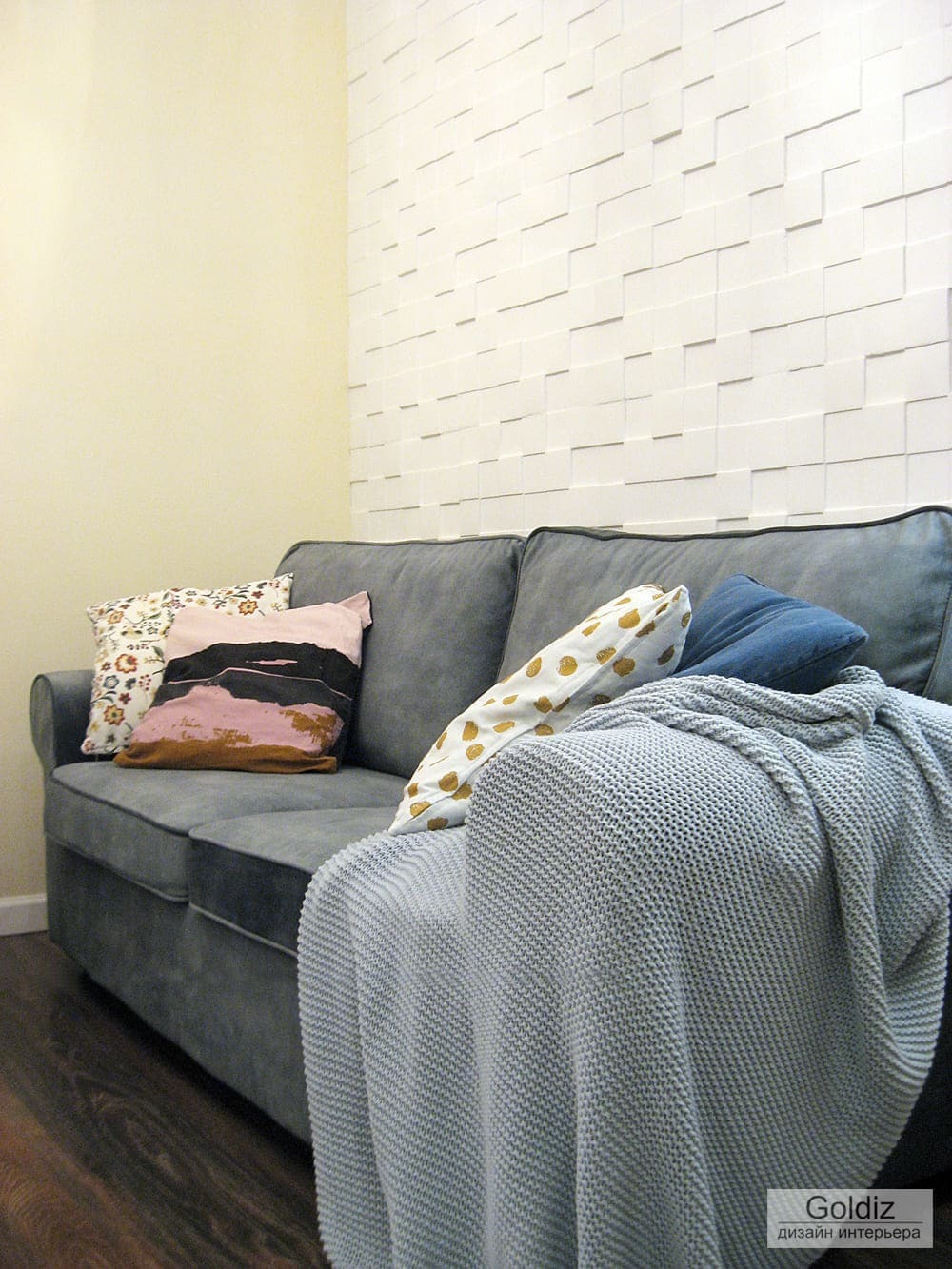 Интерьер гостиной с объемной белой декоративной стеной, серым диваном, цветными подушками и пледом &mdash; уютный современный стиль