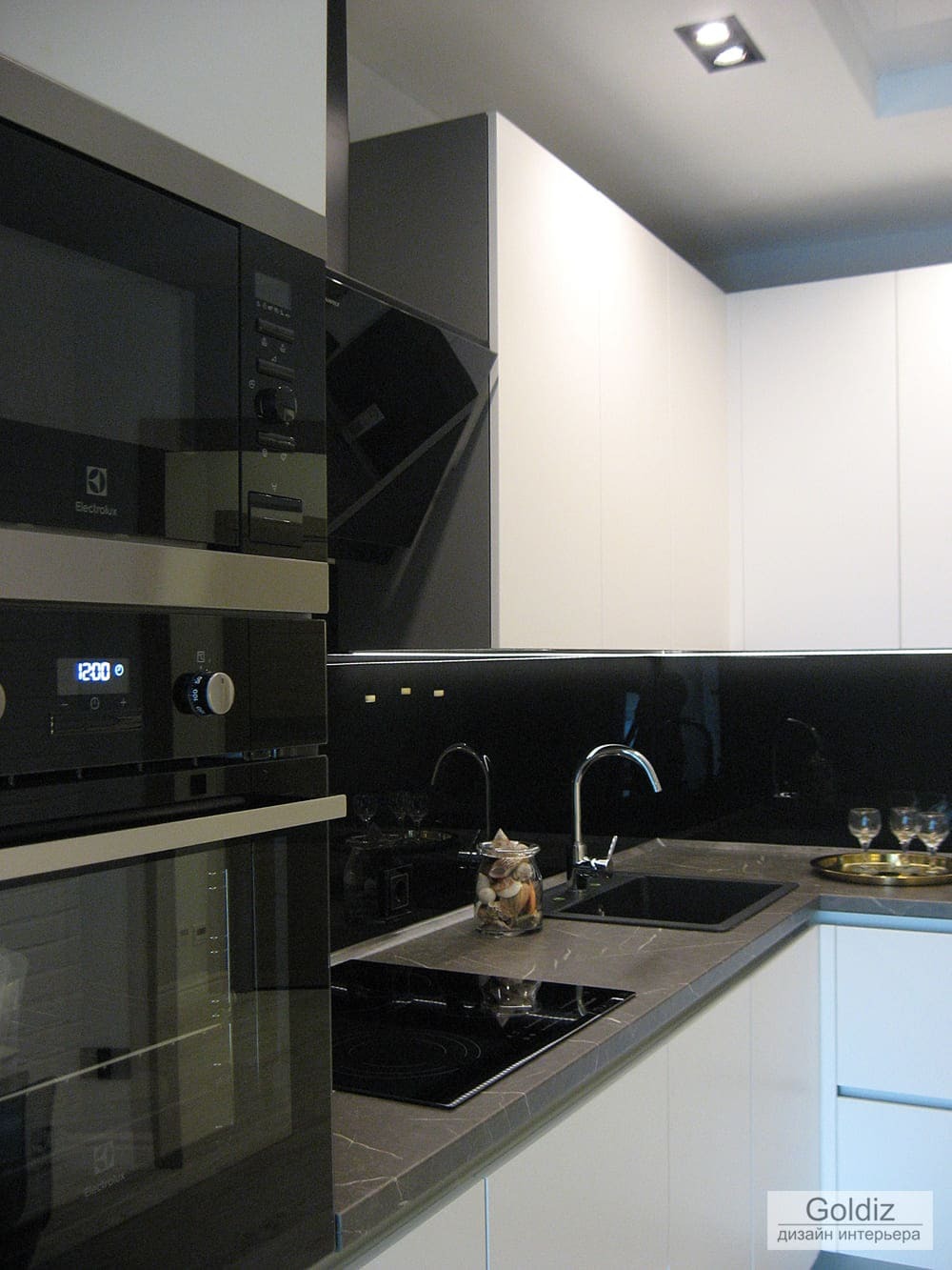 Ближний план кухни: чёрная стеклянная панель, встроенная техника Electrolux и рабочая поверхность с нейтральной текстурой