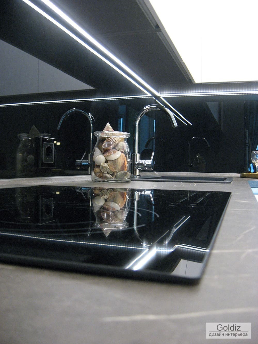 Современная кухня с чёрным стеклянным фартуком, встроенной светодиодной подсветкой и варочной панелью на керамогранитной столешнице