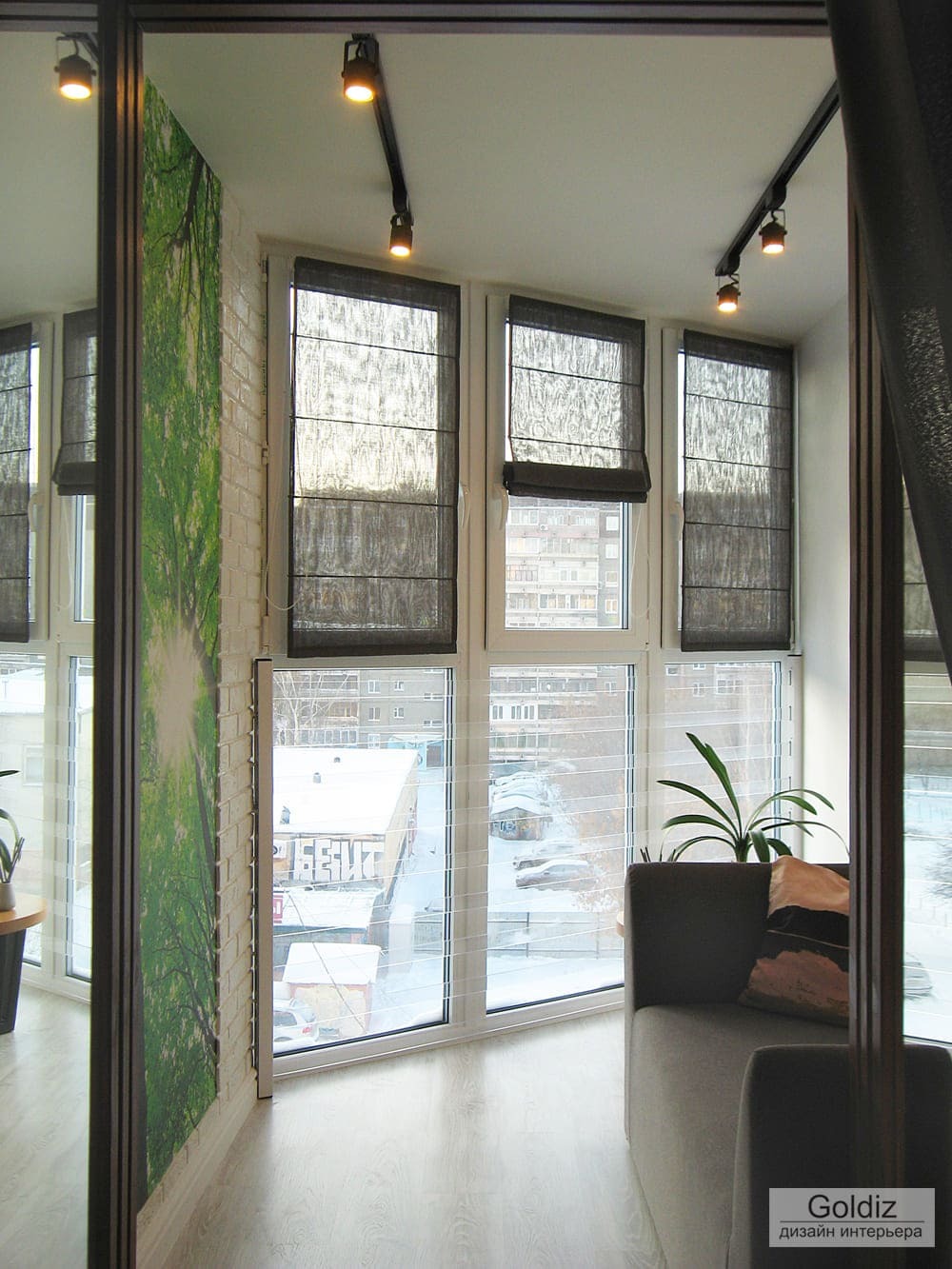 Панорамная лоджия с рулонными шторами, трековой системой освещения и зелёной декоративной панелью на стене