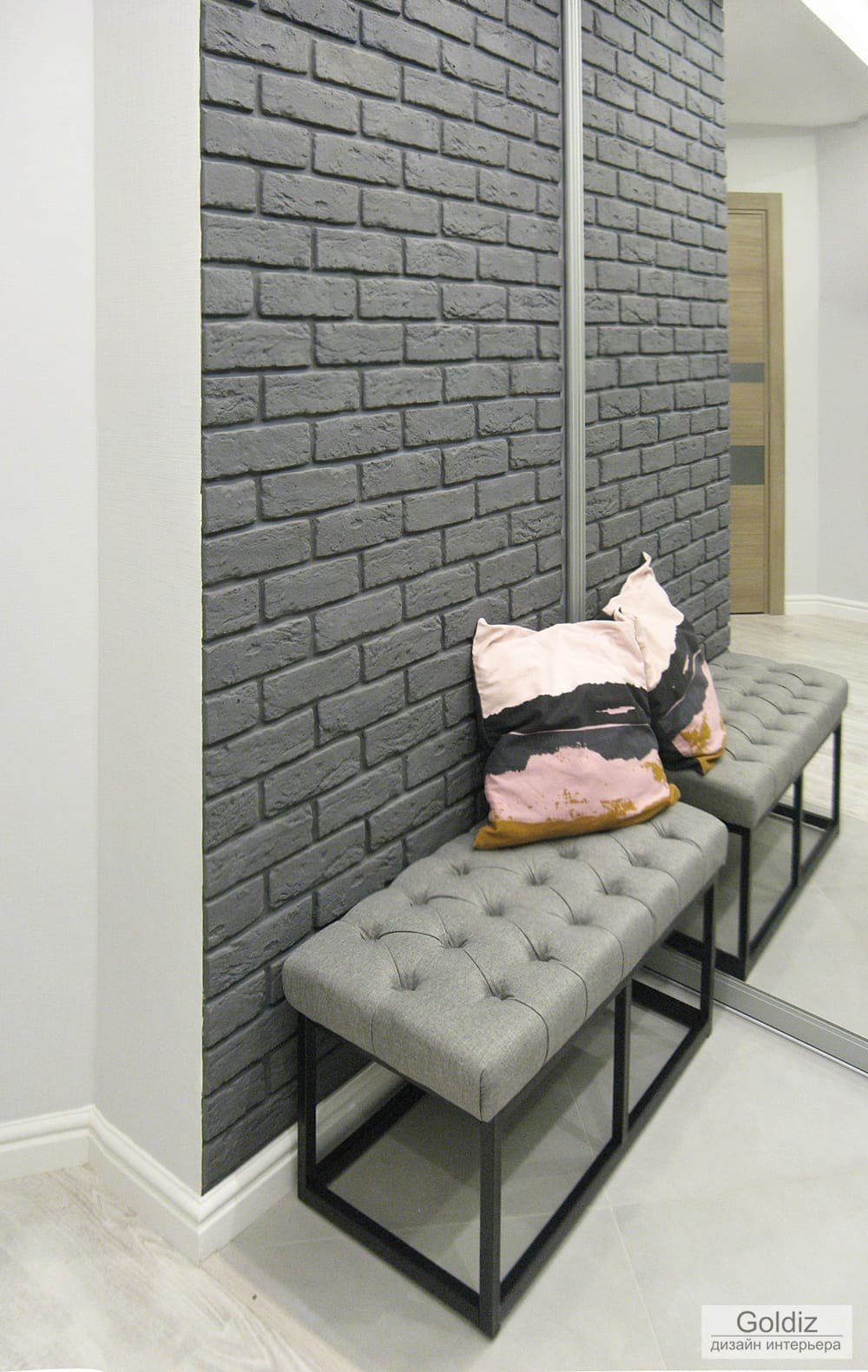 Современная прихожая с декоративной серой кирпичной стеной, мягкой банкеткой и зеркальным шкафом-купе