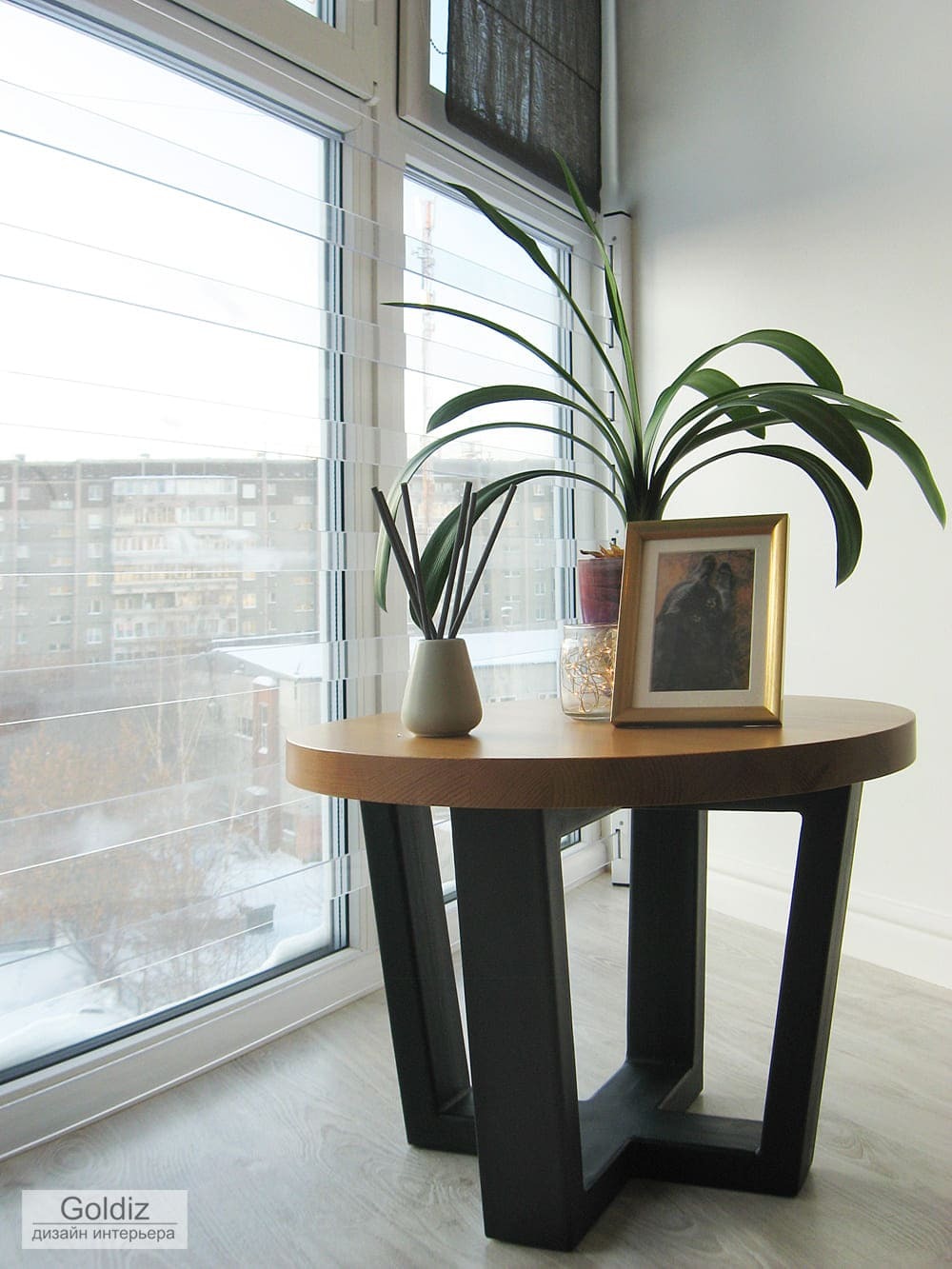 Круглый стол на лоджии с декоративным растением и широкими панорамными окнами, обеспечивающими естественное освещение