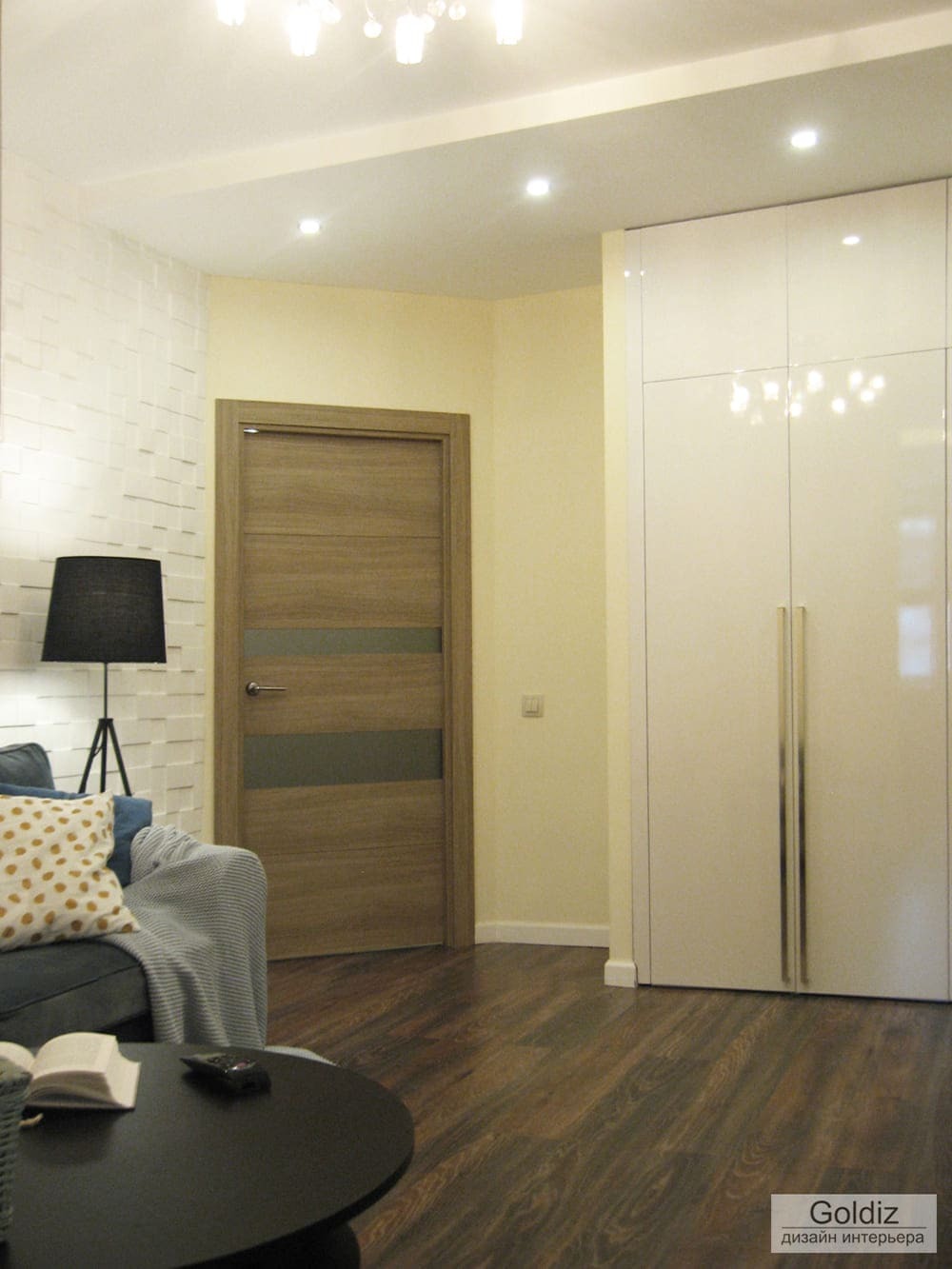 Светлая гостиная с высоким встроенным шкафом, деревянной дверью, мягким освещением и элементами современного дизайна