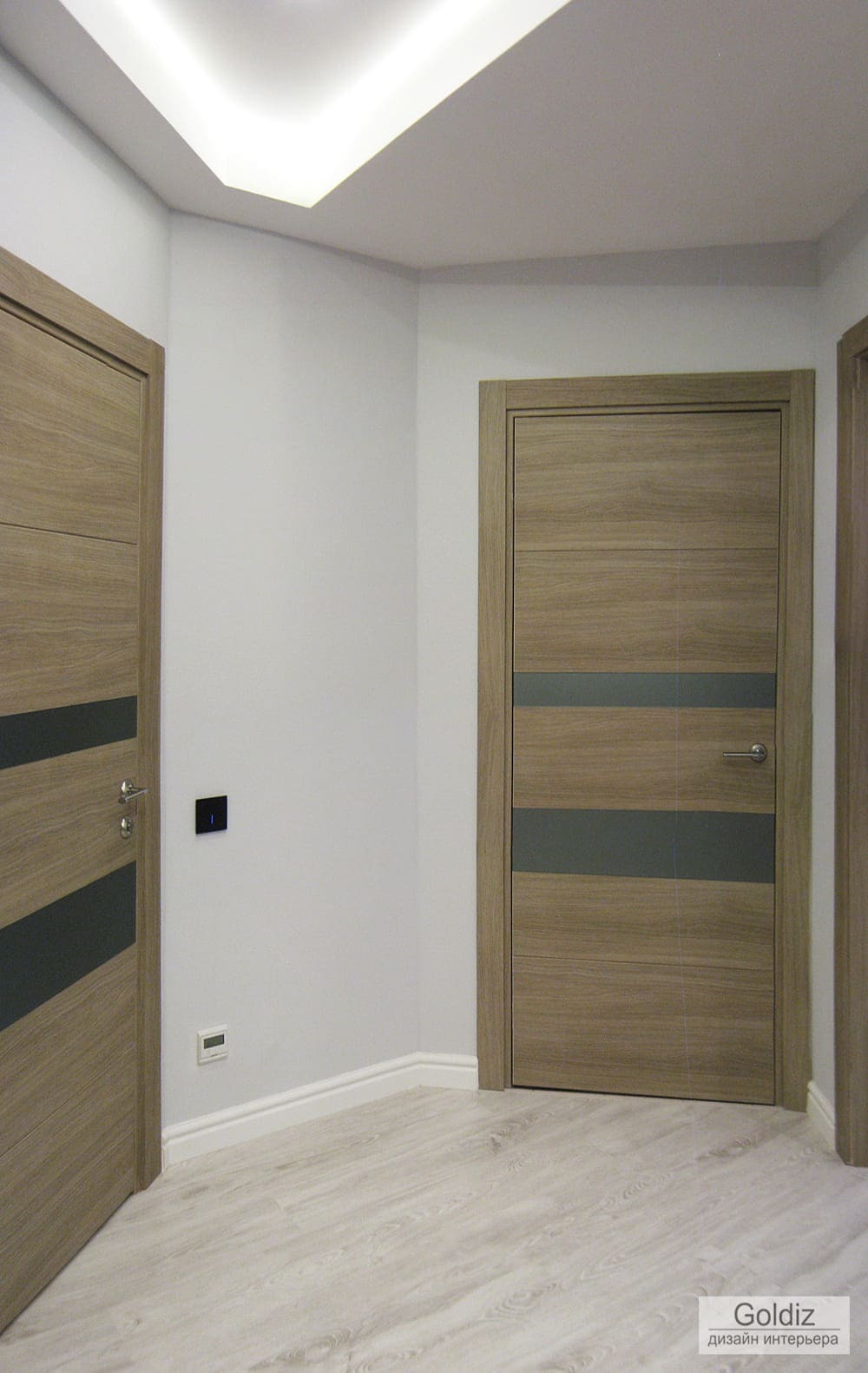Светлая прихожая с деревянными дверями, геометрией потолка и встроенной светодиодной подсветкой
