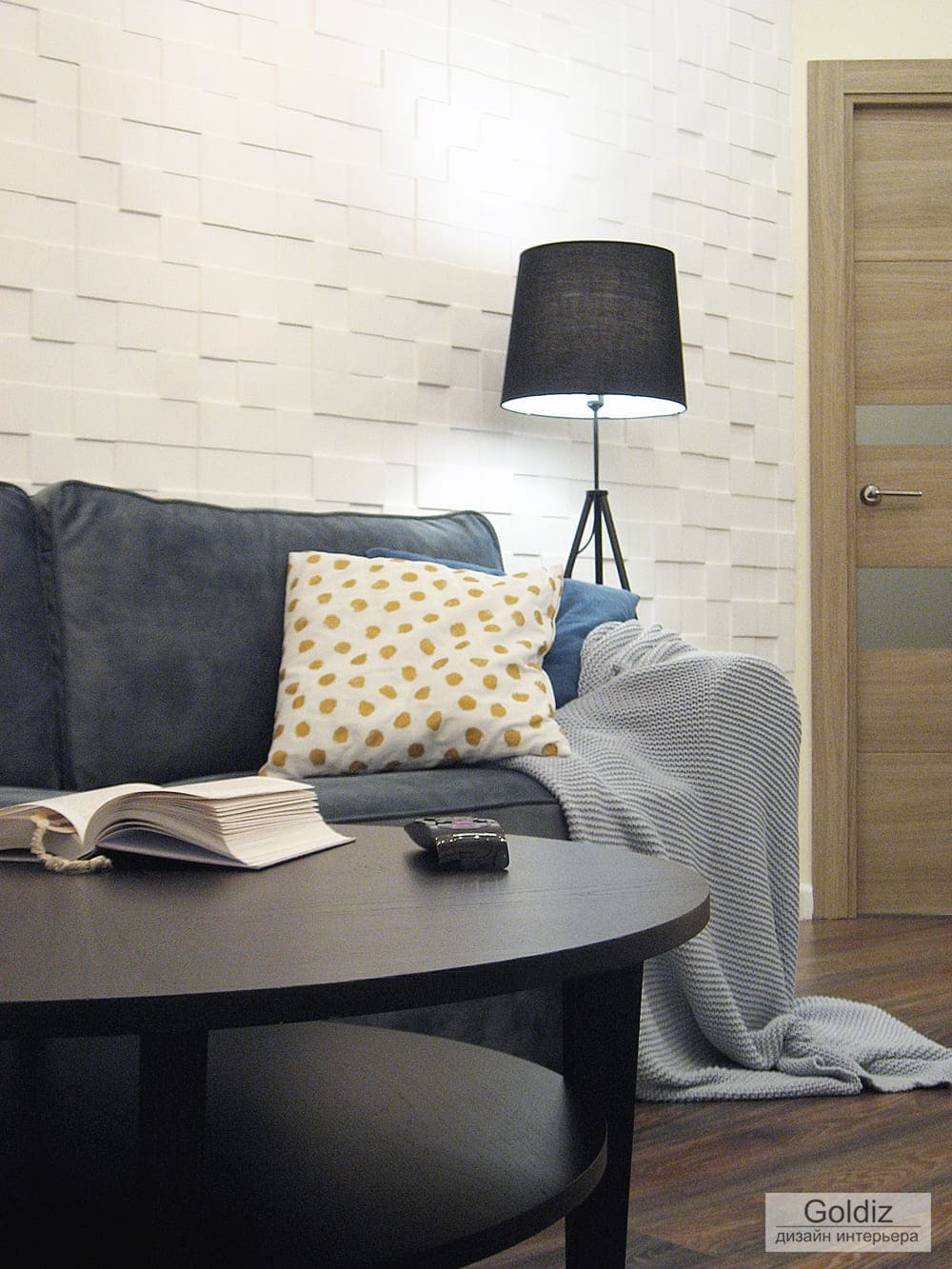 Уютная гостиная с серым диваном, декоративной объемной стеной, черным торшером и журнальным столиком &mdash; современный интерьер квартиры