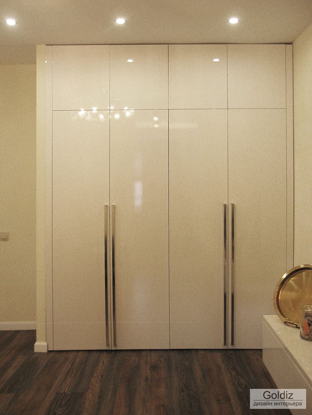 Встроенный глянцевый белый шкаф в интерьере гостиной, с точечной подсветкой и деревянным полом &mdash; минималистичное современное решение
