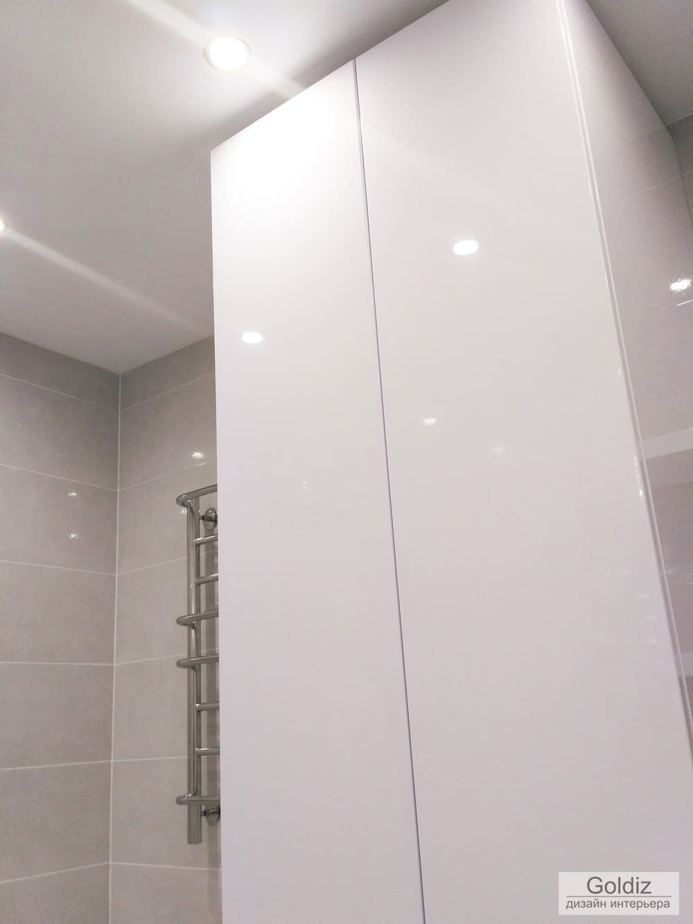 Белый высокий глянцевый шкаф в ванной комнате, встроенное освещение и спокойная светлая плитка &mdash; современный дизайн квартиры