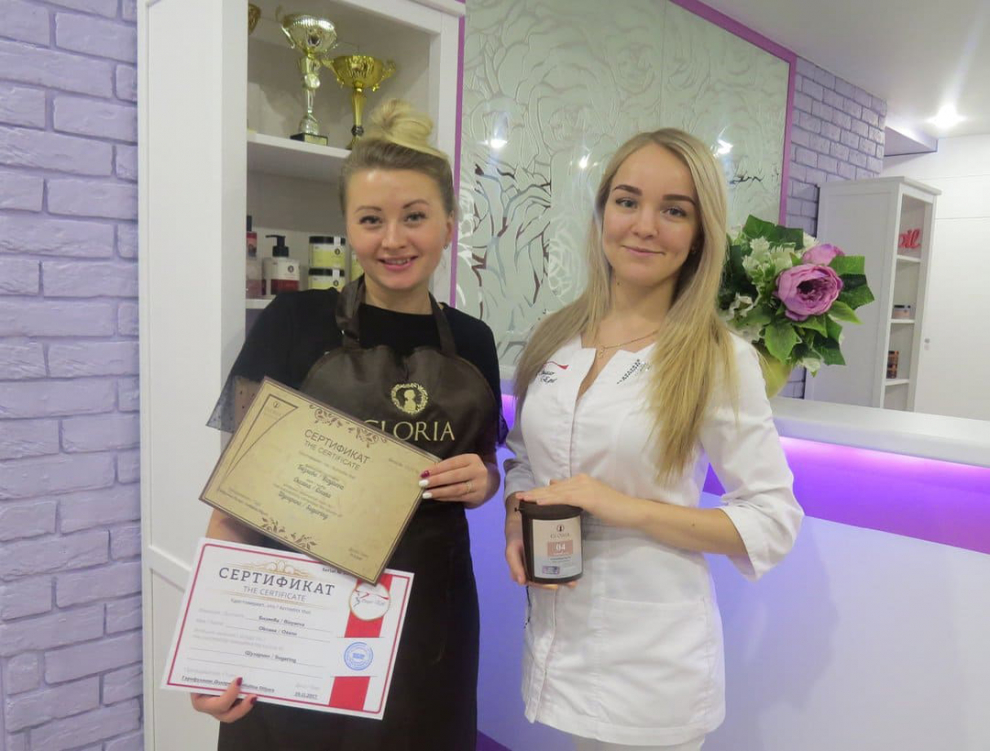 Сотрудник салона с сертификатом и продуктами для ухода за кожей, подчеркивающими высокую квалификацию и заботу о клиентах.