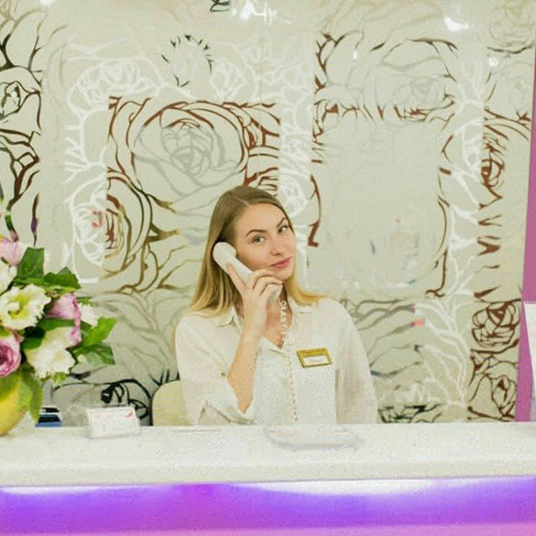 Работник салона на ресепшн, принимающий звонок. На переднем плане стильные цветы и современная мебель, создающие гармоничную атмосферу