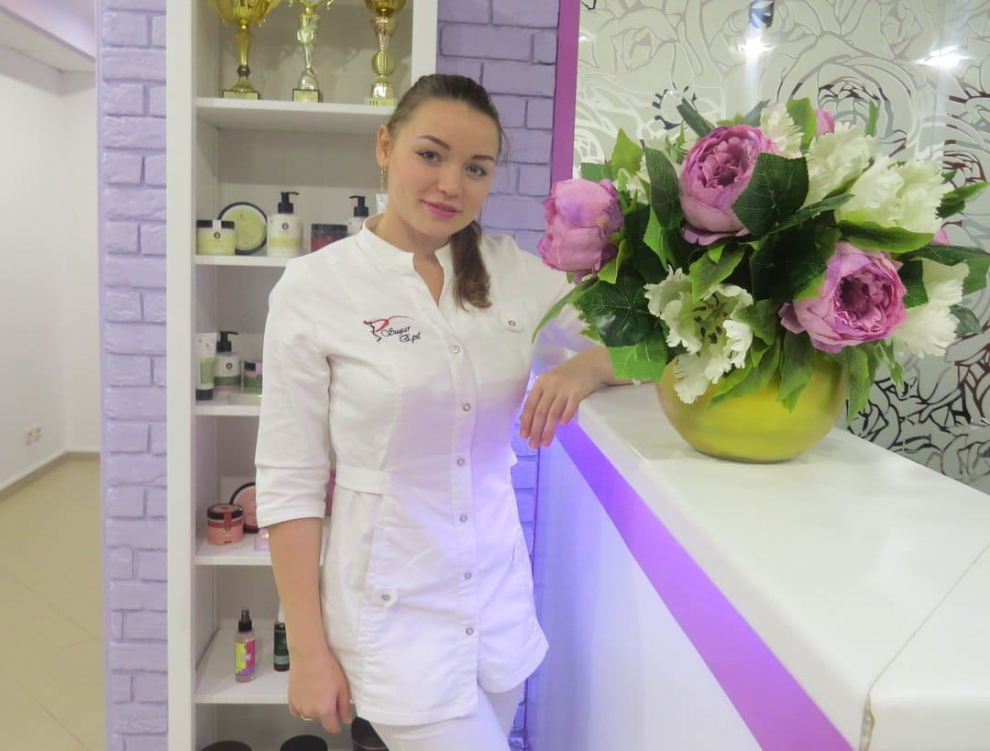 Работник салона красоты на фоне стильного ресепшн с яркими цветами, отражающий атмосферу уюта и профессионализма.